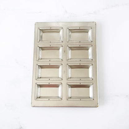 Silicone-coated metallic financier pan with eight square compartments on a white background