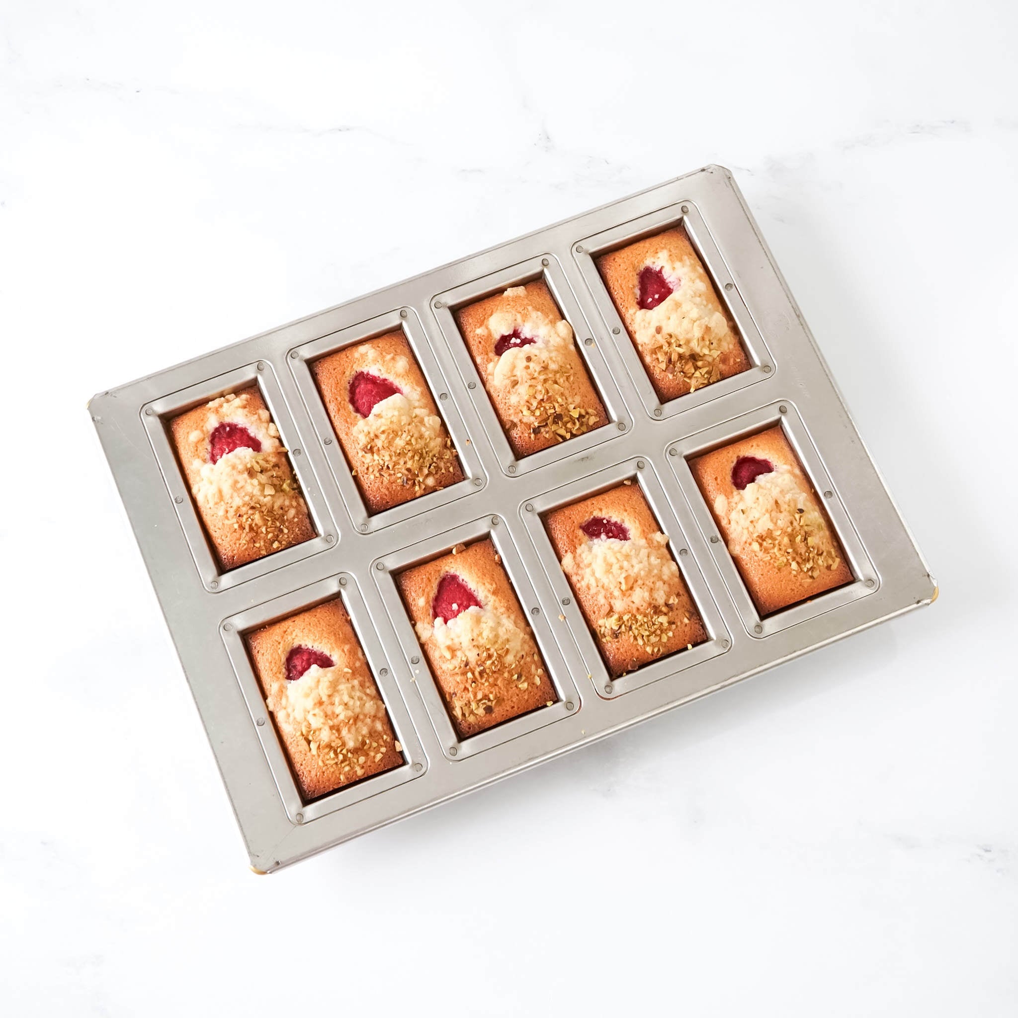 Baked goods in a metal financier mold on a white background