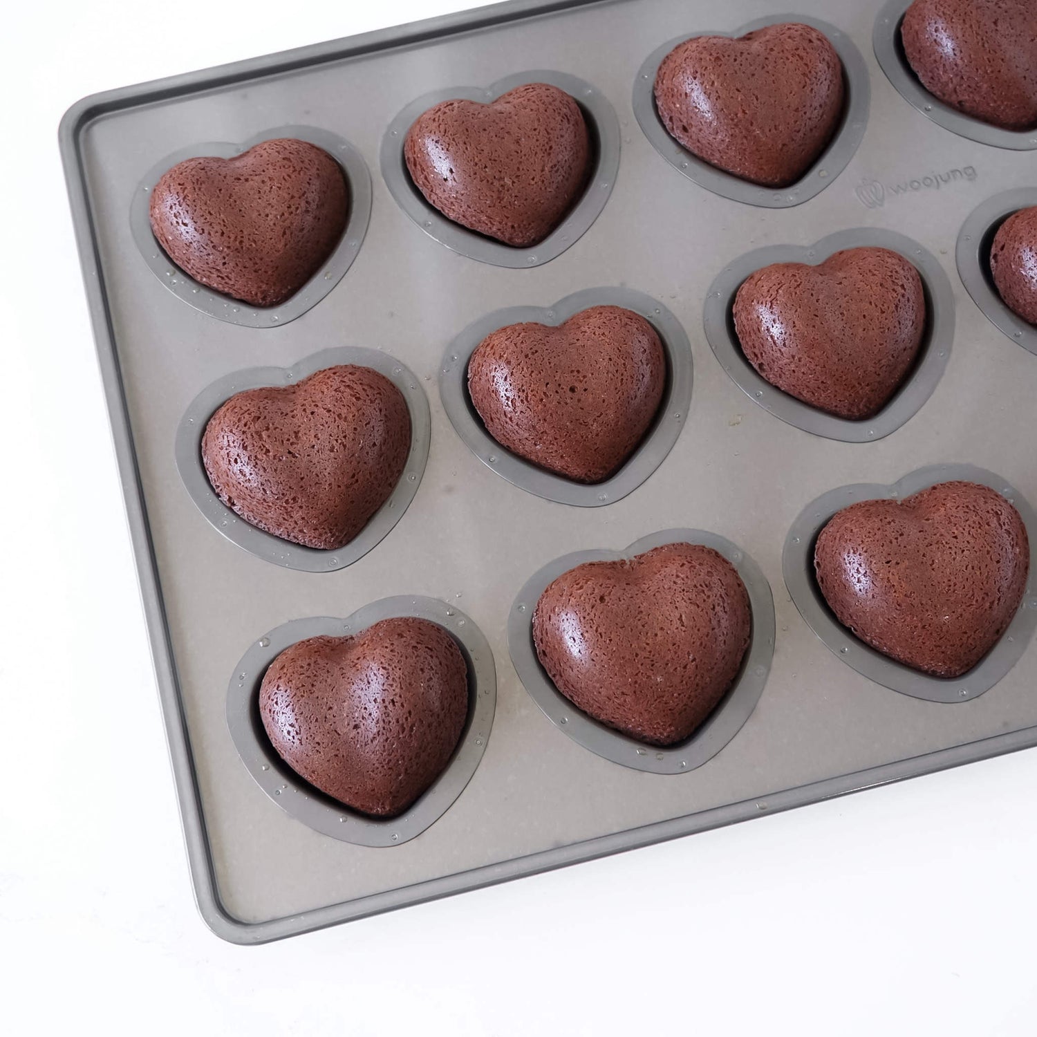 A heart-shaped silicone mold tray containing several baked chocolate brown heart-shaped cakes, shown on a clean white background.