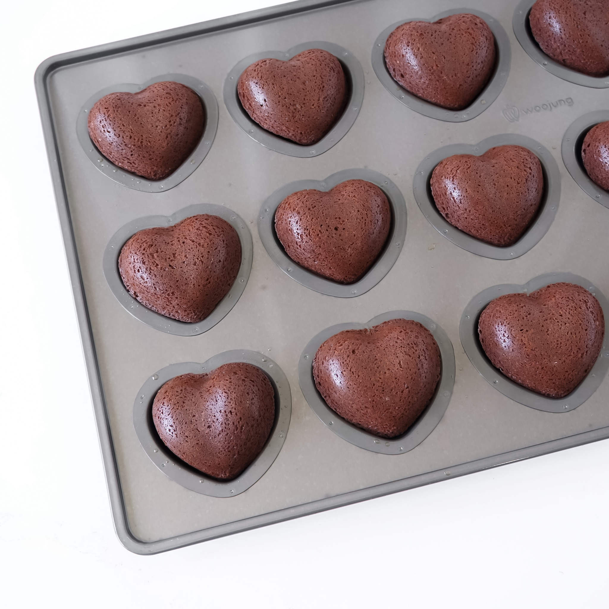 A heart-shaped silicone mold tray containing several baked chocolate brown heart-shaped cakes, shown on a clean white background.