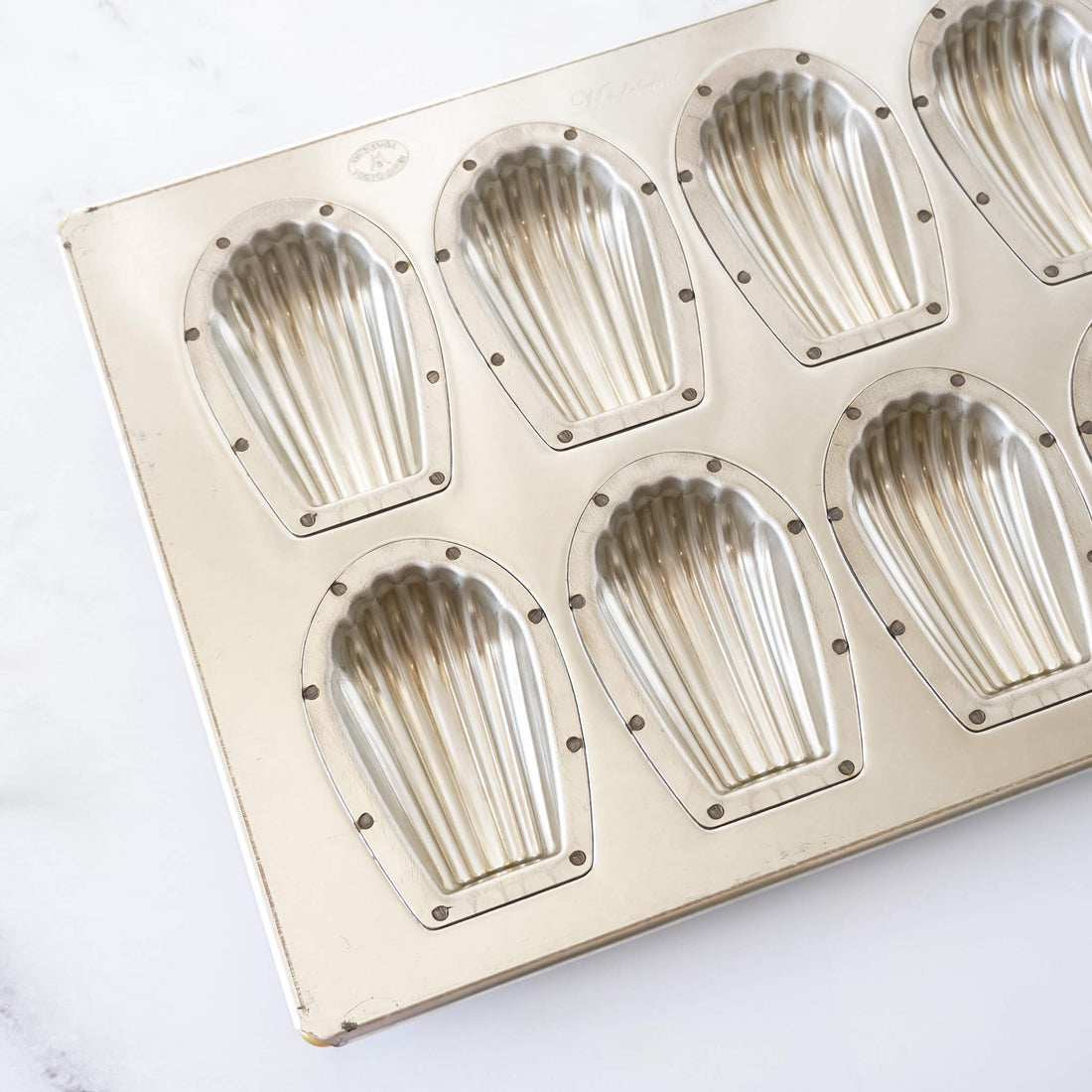 Metallic madeleine mold with shell-shaped cavities on a white background