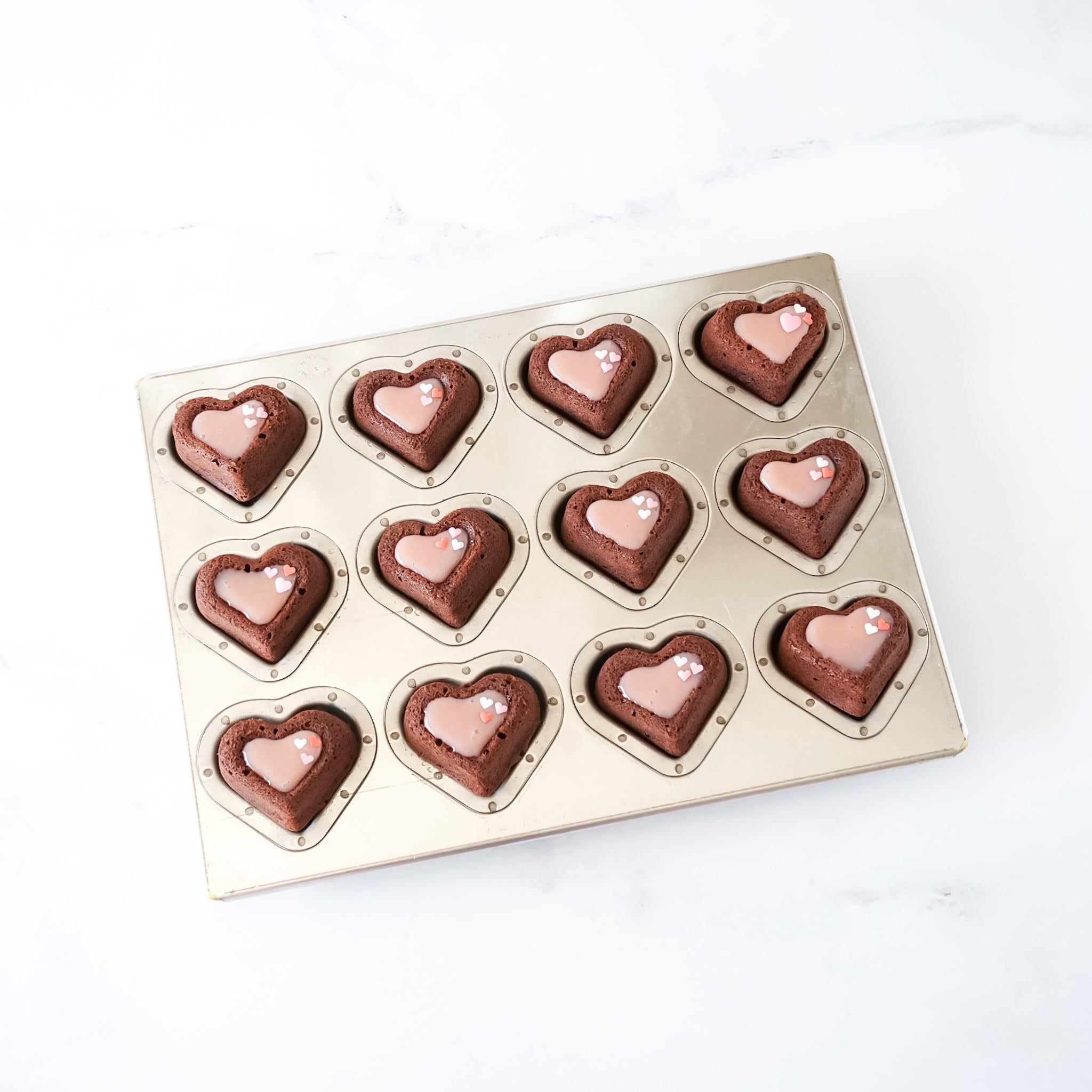 A silicone-coated madeleine pan with double heart-shaped cavities, displaying baked madeleines on a white background.