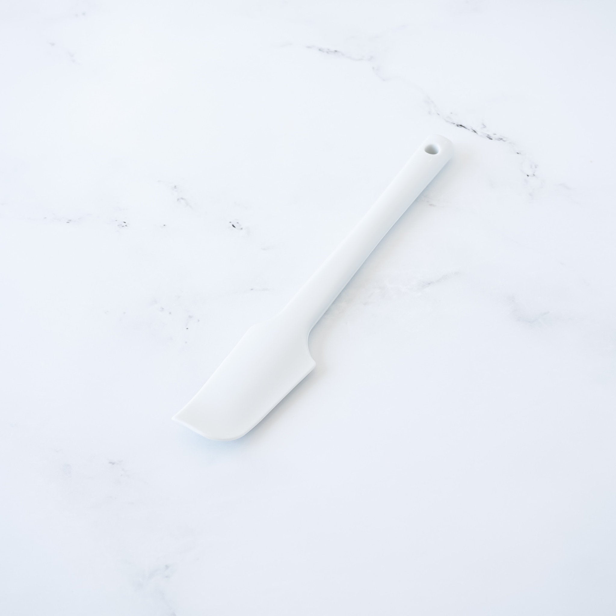 A white silicone spatula with a rounded tip and a long handle.