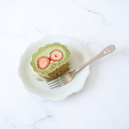Slice of matcha roll cake with strawberries on a white plate with a fork.