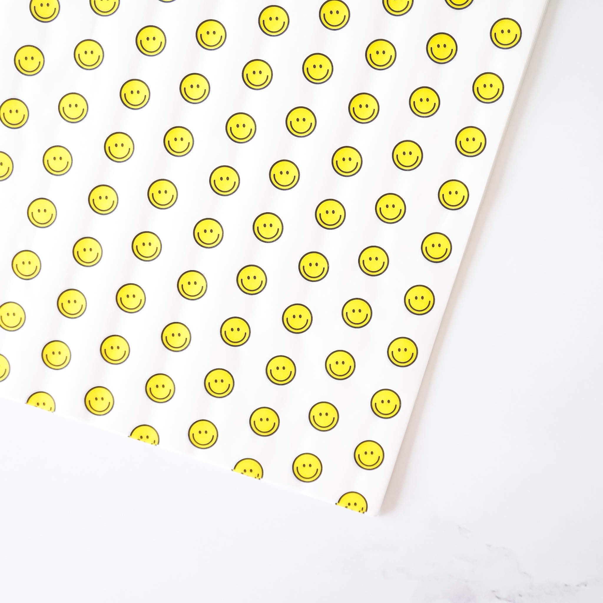 A sheet of deli paper with a yellow smiley face pattern on a white background, presumably made of coated parchment paper.
