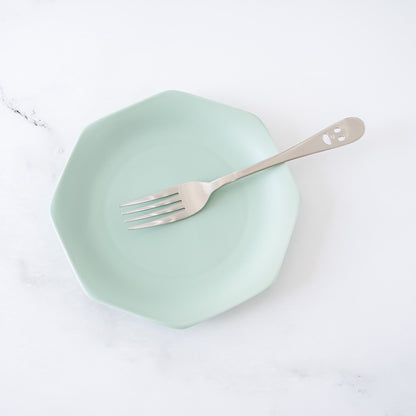 Mint green plate with a fork on a white marble surface