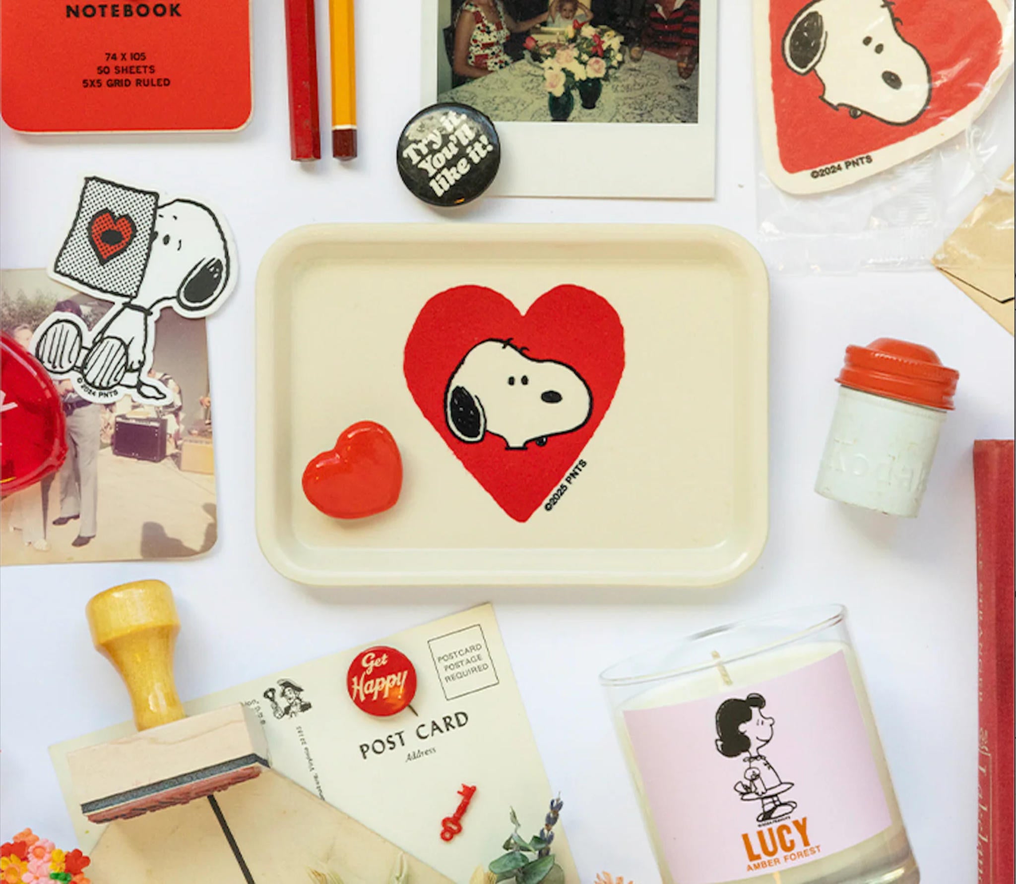 Collection of Snoopy-themed products including a tray, postcards, and a candle on a white background.