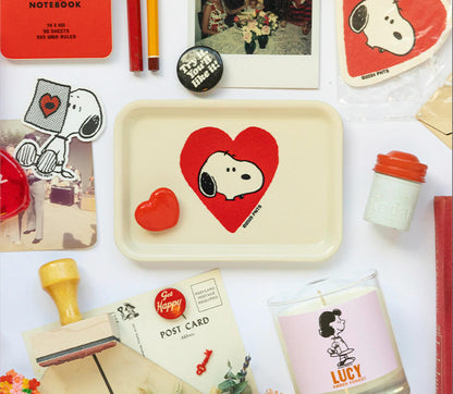 Collection of Snoopy-themed products including a tray, postcards, and a candle on a white background.