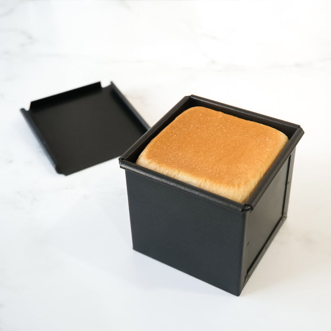 Square piece of bread in a black loaf pan on a white background
