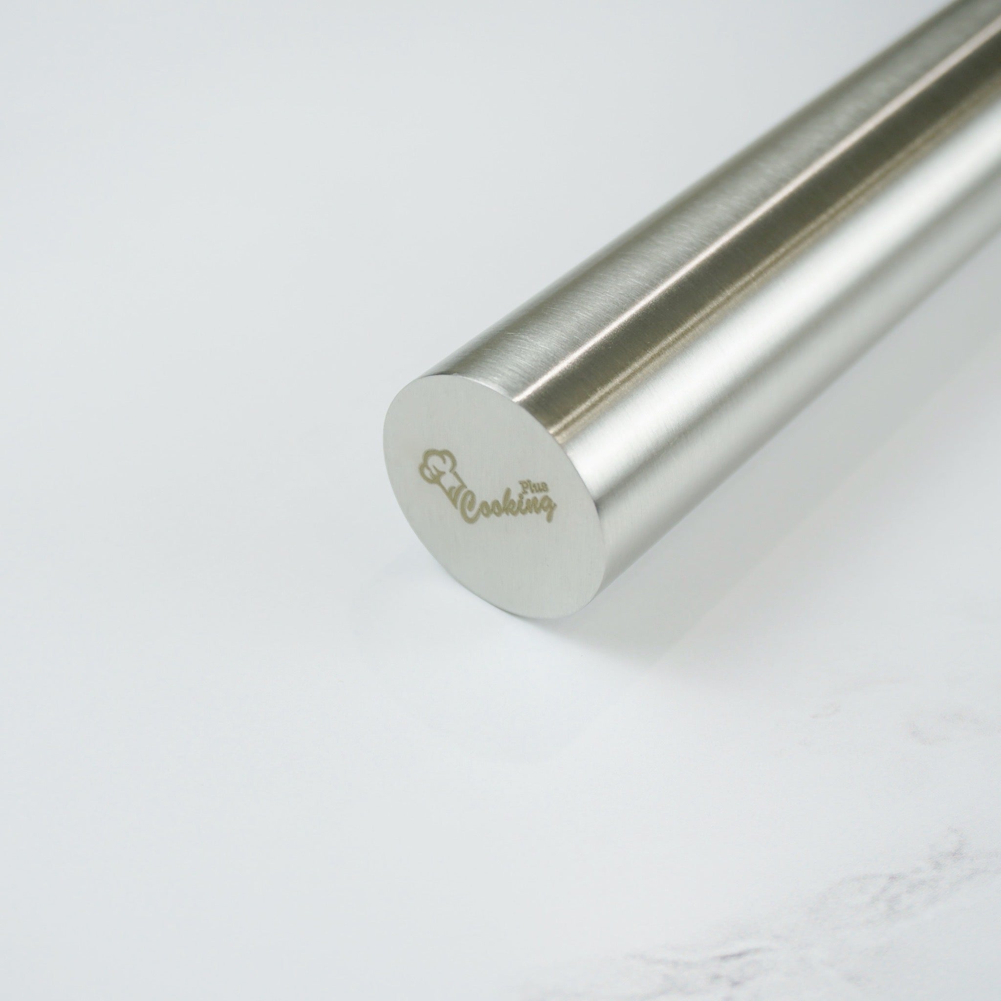 A stainless steel metal rolling pin on a white marble surface.