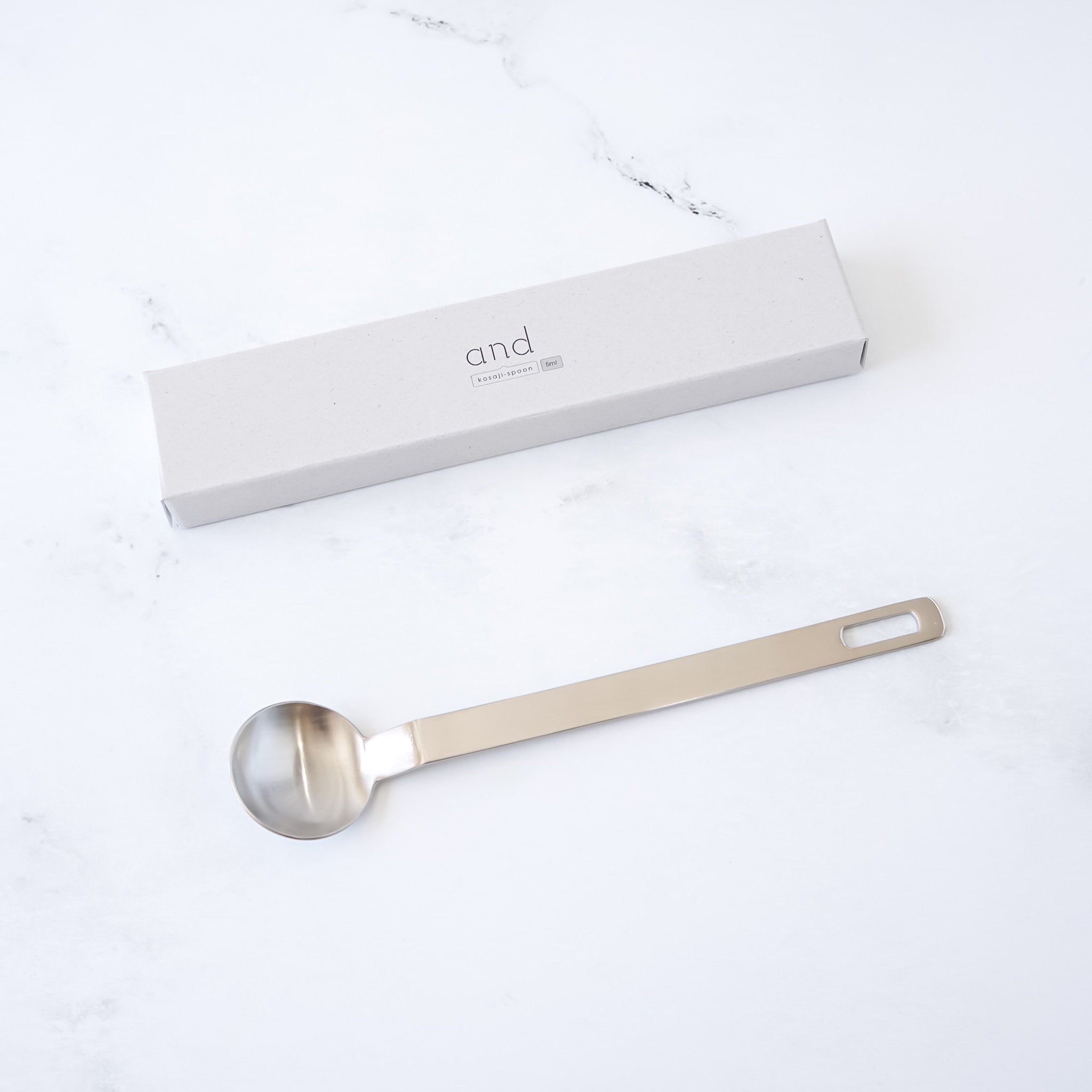 Stainless steel teaspoon with a branded box on a white surface