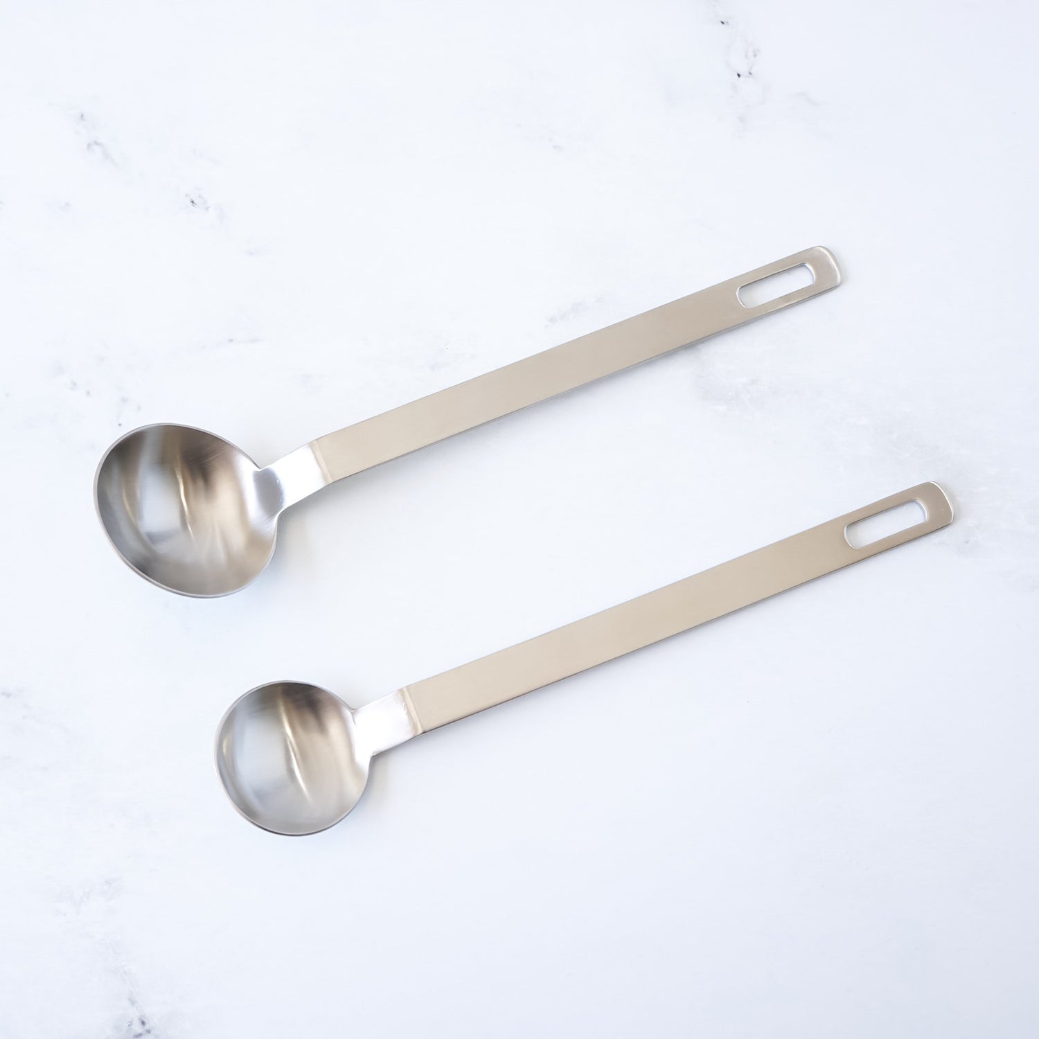 Two stainless steel measuring spoons on a white background