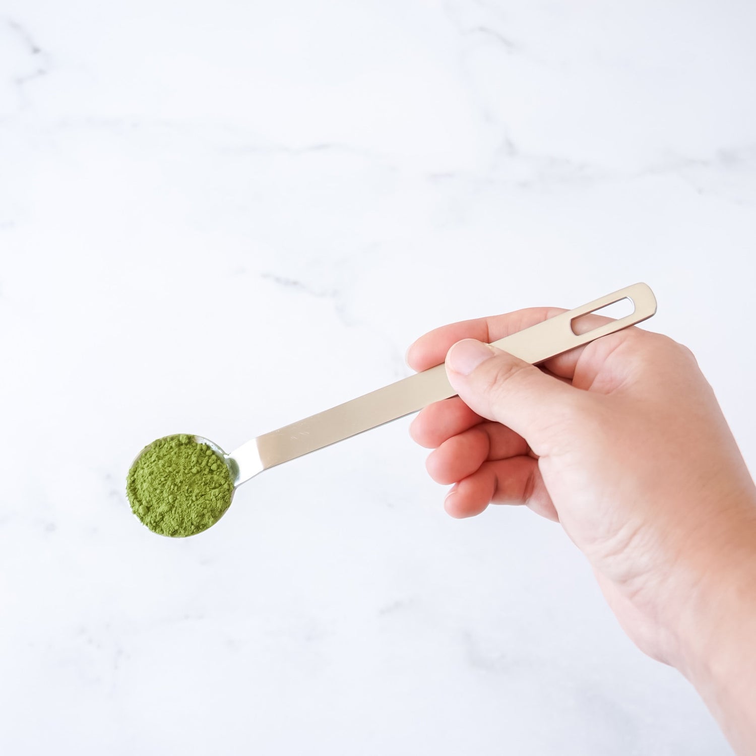 Hand holding a teaspoon with green tea powder on a white background