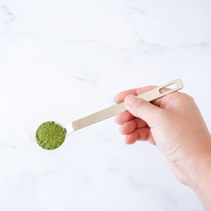 Hand holding a teaspoon with green tea powder on a white background
