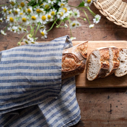 Sliced bread on a wooden cutting board with a blue and linen striped towel and flowers in the background.