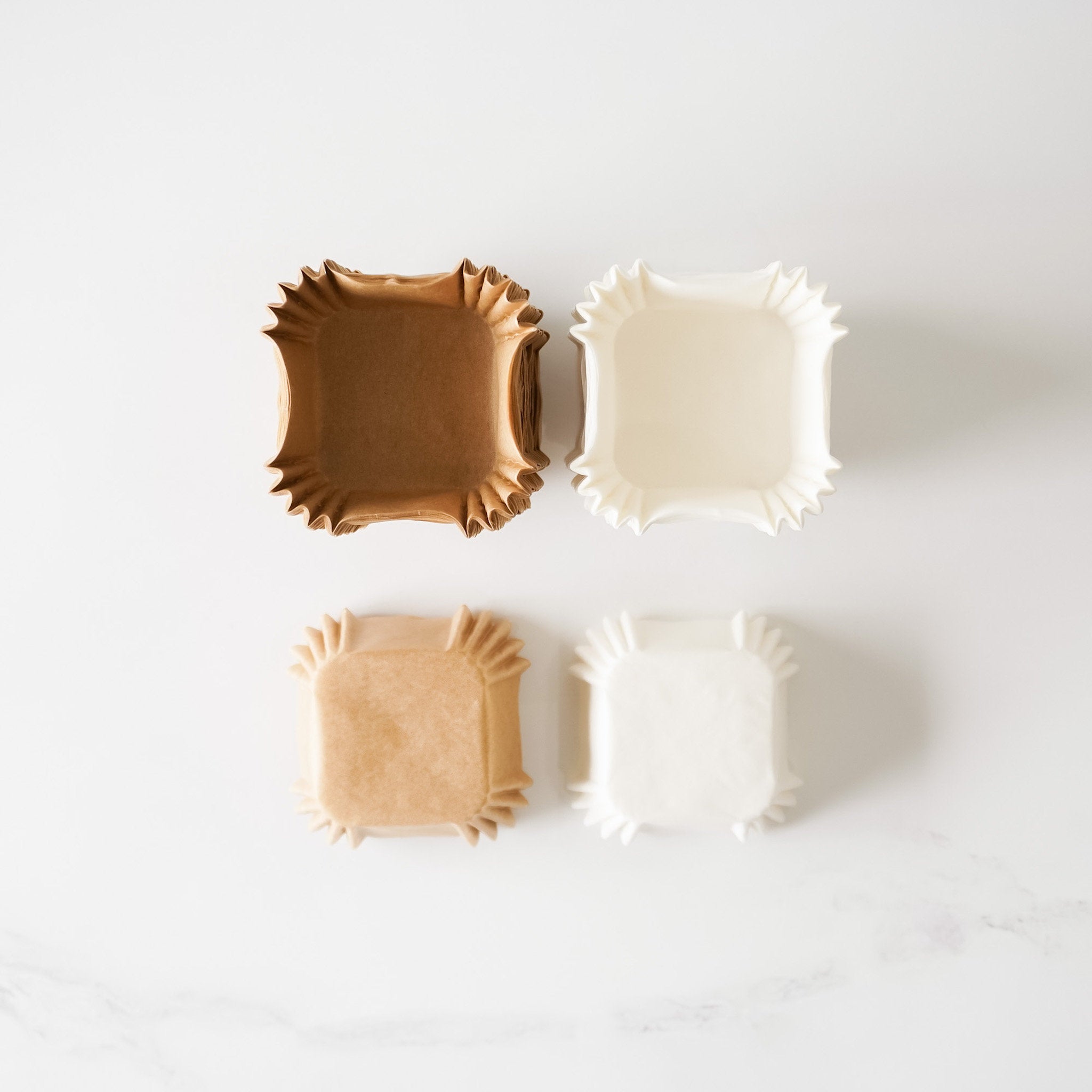 Four paper cupcake liners, two are brown and two are white. The liners are arranged in two rows of two, with the brown liners on top and the white liners on the bottom.