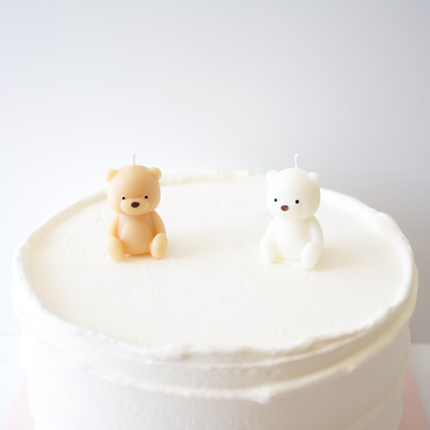 Two bear-shaped candles on a white cake against a light gray background