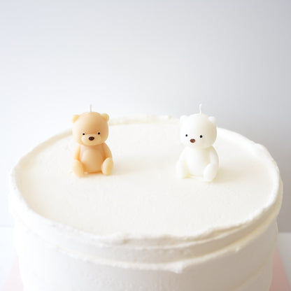 Two bear-shaped candles on a white cake against a light gray background