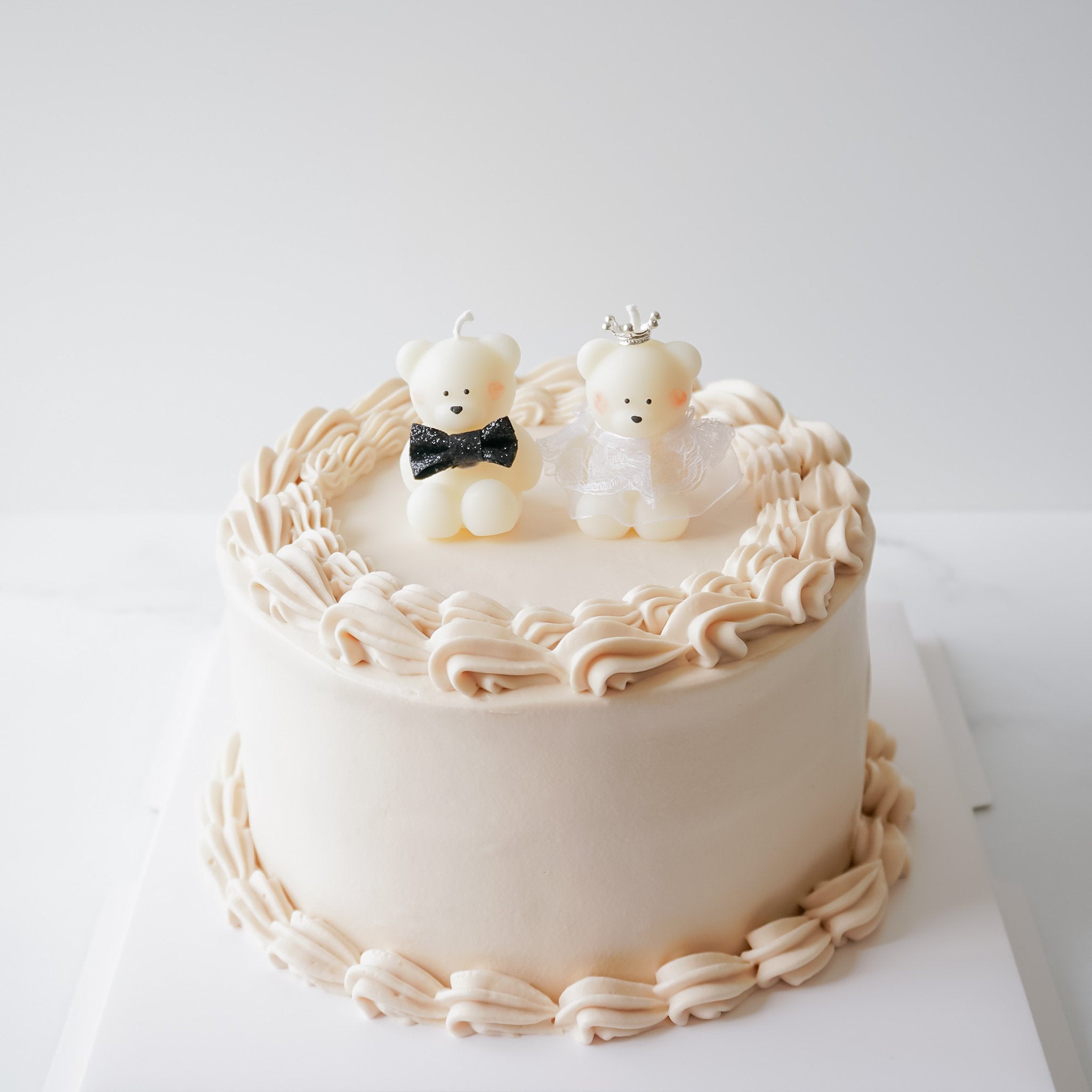 A decorative cake candle topper featuring a bride and groom bear design, placed on a wedding cake with white icing.