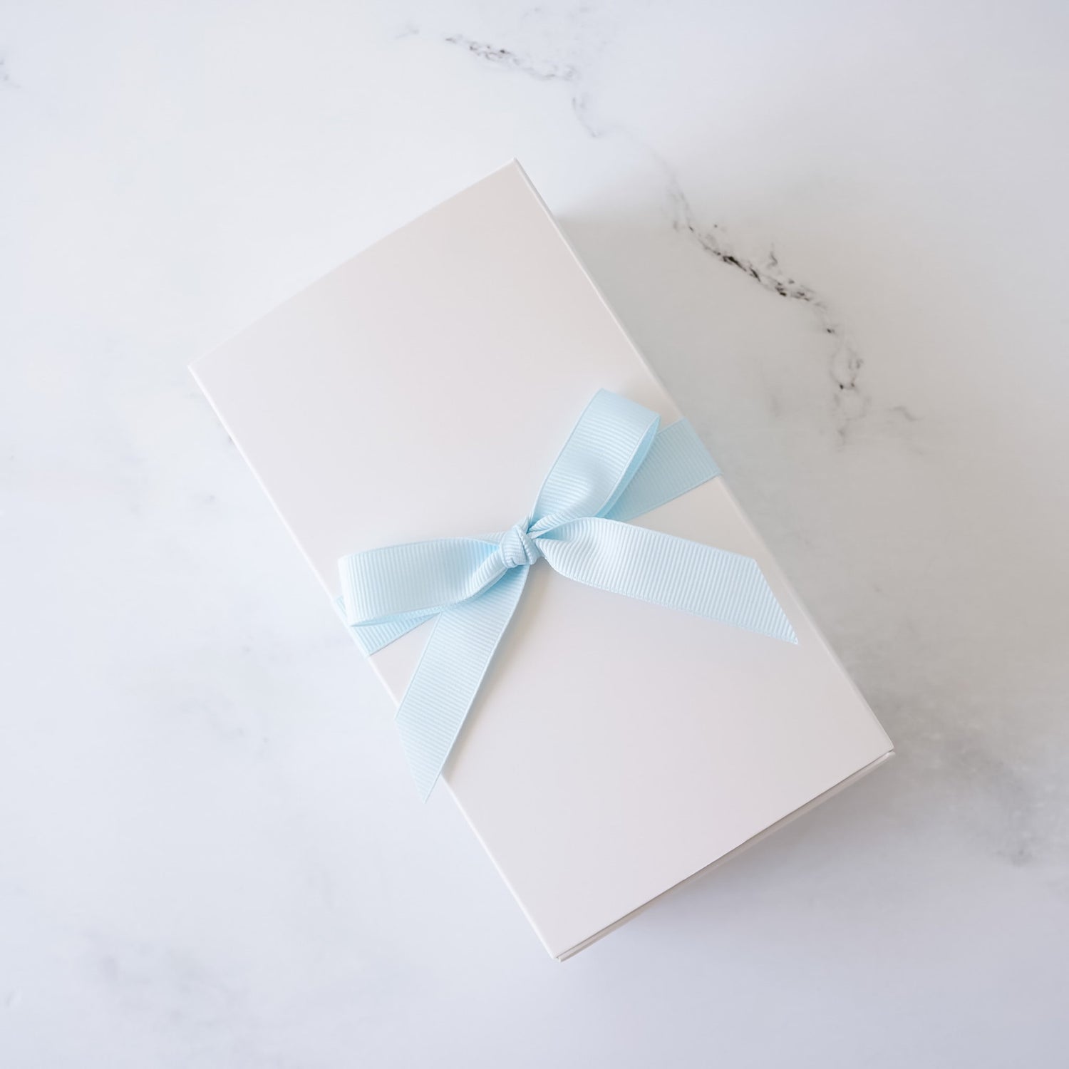 White cookie box with a light blue ribbon on a marble surface