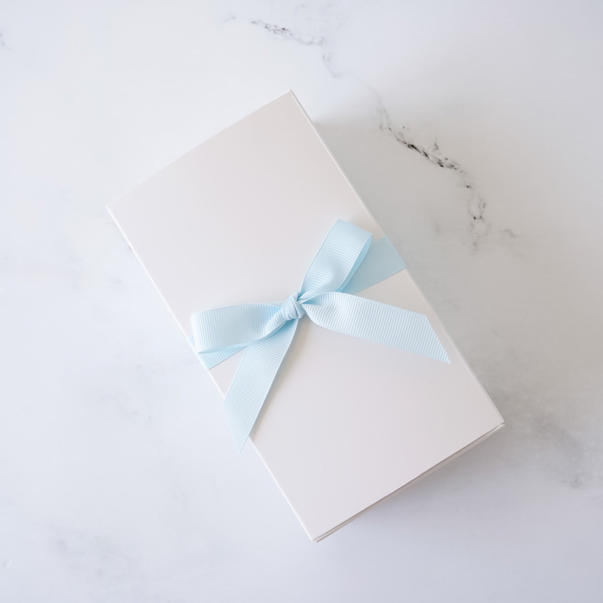 White cookie box with a light blue ribbon on a marble surface