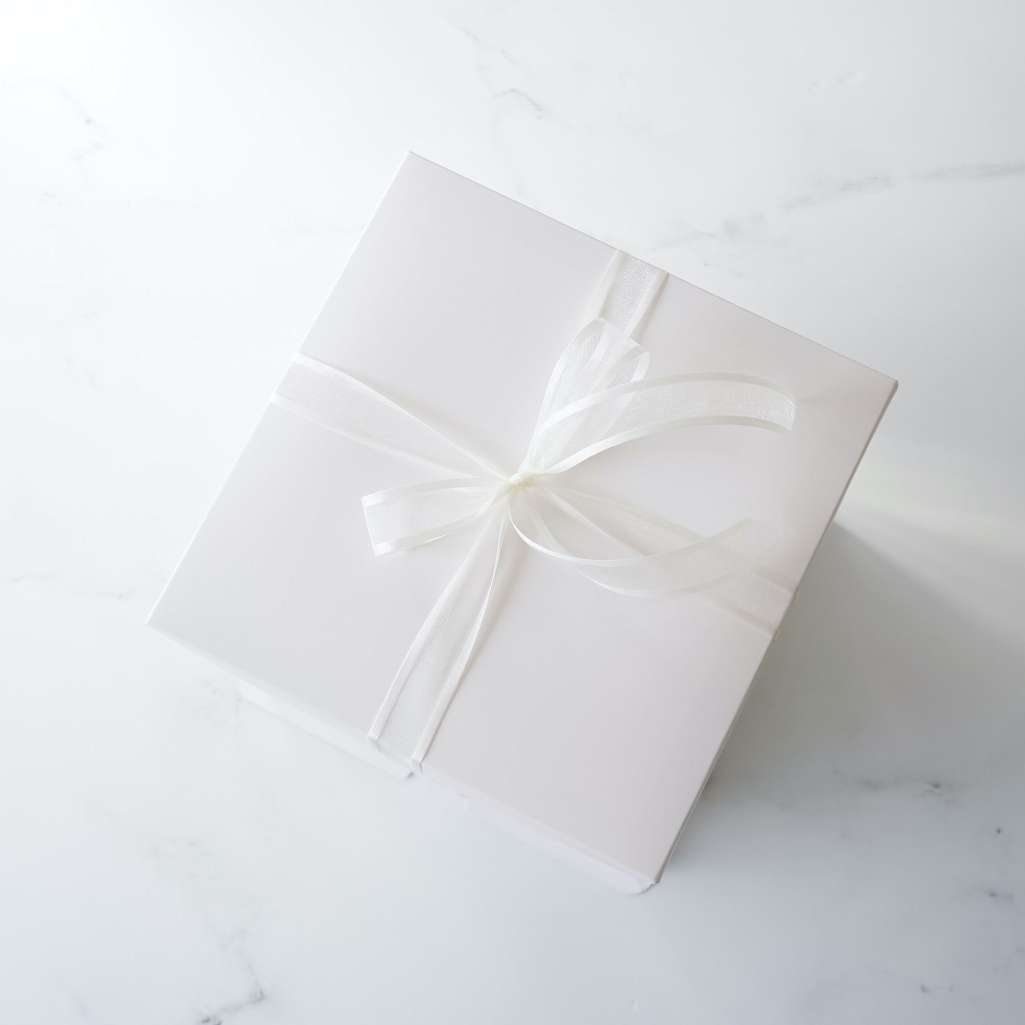 A white square gift box with a white satin ribbon tied in a bow on top.
