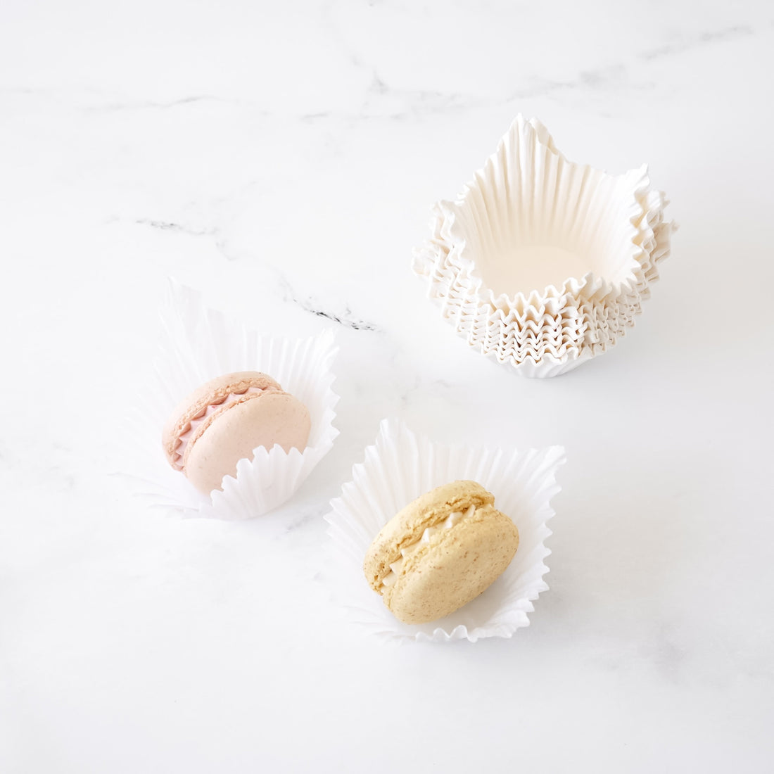 Two macarons in white paper cups on a light background