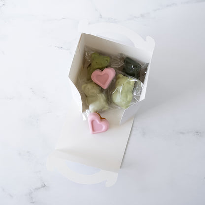 White bakery box with heart-shaped pink and green madeleines on a marble surface
