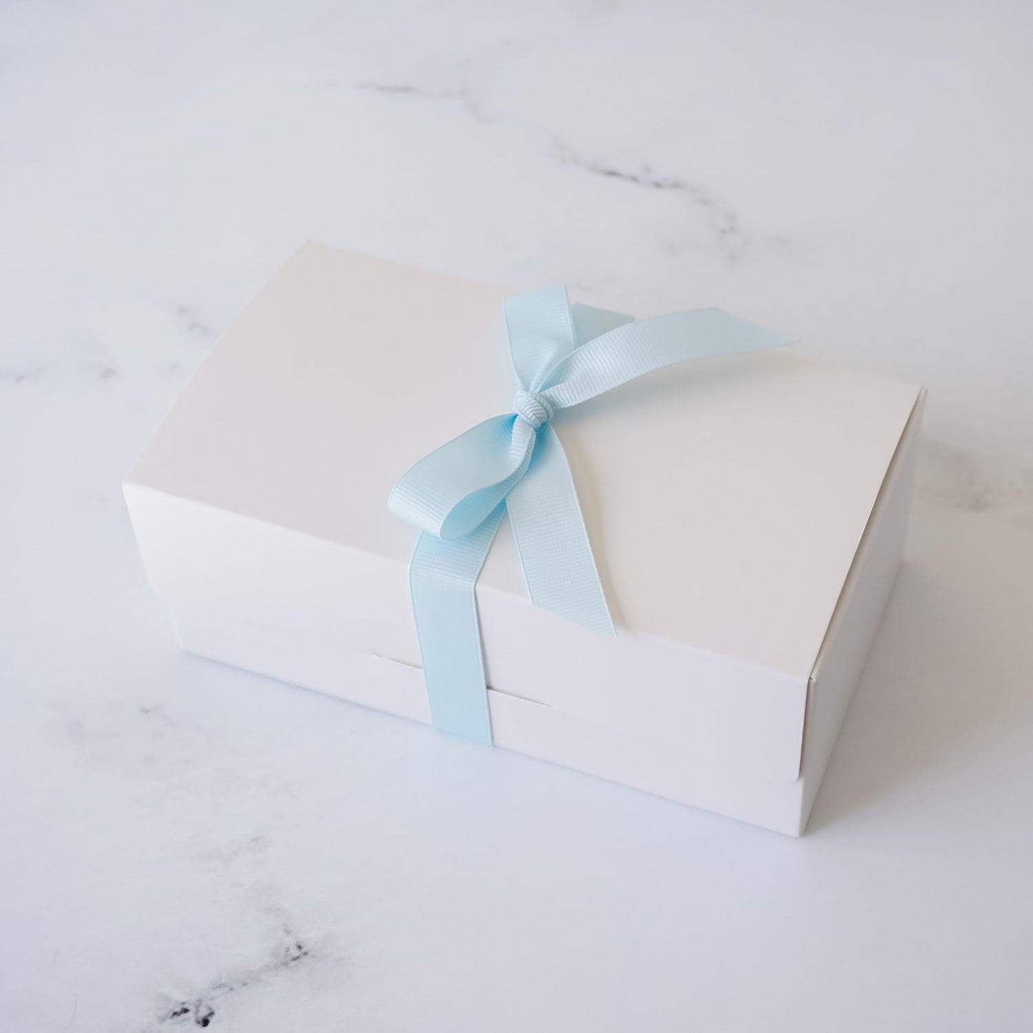 White bakery box with a light blue ribbon on a marble surface