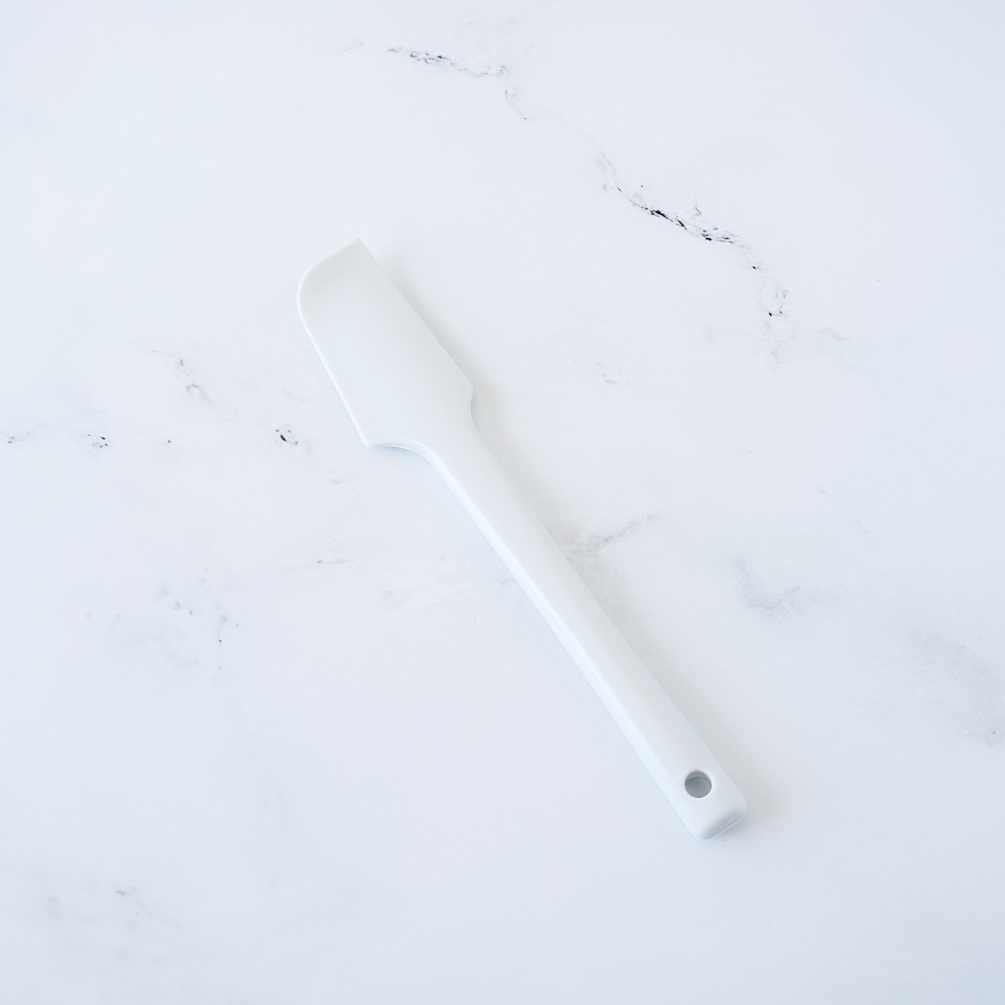 A white silicone spatula with a rounded edge and a hole in the handle
