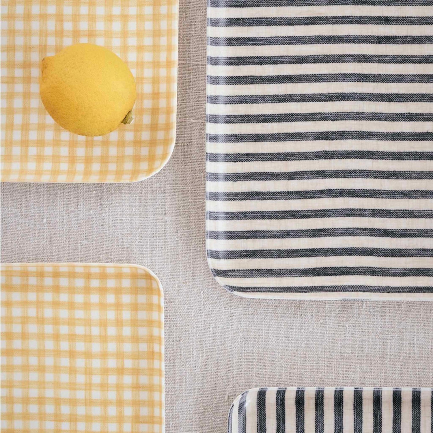 Two yellow checkered trays with a lemon on one and a black and white striped tray on a gray surface.