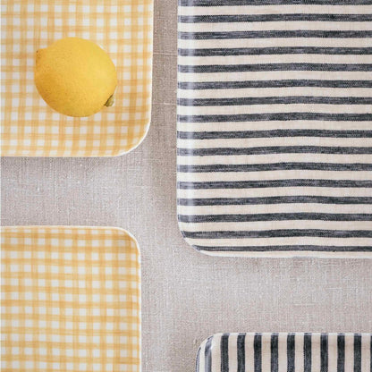 Two yellow checkered trays with a lemon on one and a black and white striped tray on a gray surface.