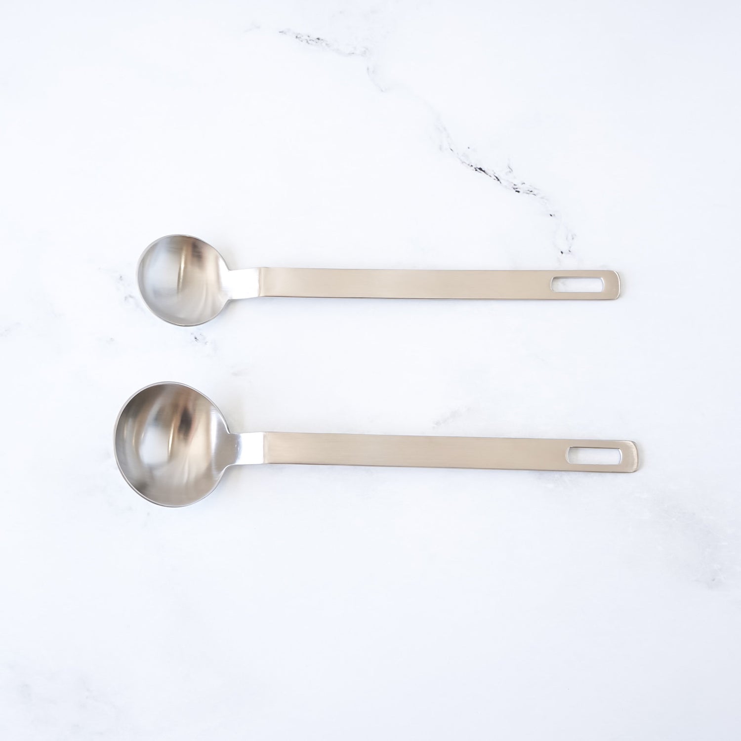 Two stainless steel measuring spoons on a white marble surface