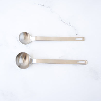 Two stainless steel measuring spoons on a white marble surface